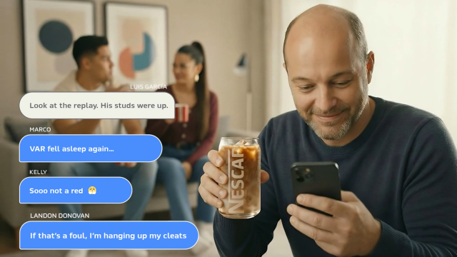 Man smiles, holding Nescafé iced coffee and iPhone, engaging in a lively sports chat with friends about a VAR decision.